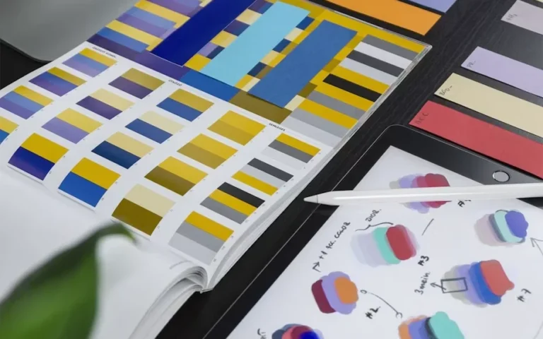 Colour swatch book, paper strips and a tablet with palette sketches on a desk